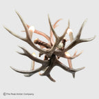 A rustic deer antler chandelier light fixture with multiple faux antler branches and built-in candle-style bulbs, shown against a light gray background. A copyright watermark for The Peak Antler Company appears in the lower-left corner.