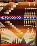 Pendleton blanket with chocolate brown, gold, cream, and green geometric patterns and a blue and red accent stripe.