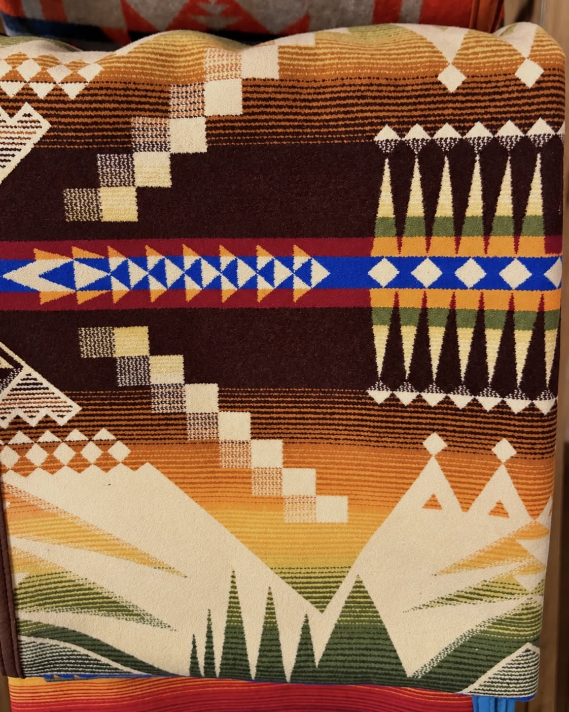 Pendleton blanket with chocolate brown, gold, cream, and green geometric patterns and a blue and red accent stripe.