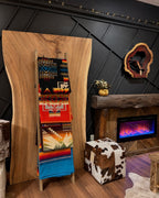 Red-orange Southwestern blanket on the second rung of a wooden display ladder beside a rustic fireplace, with other blankets.