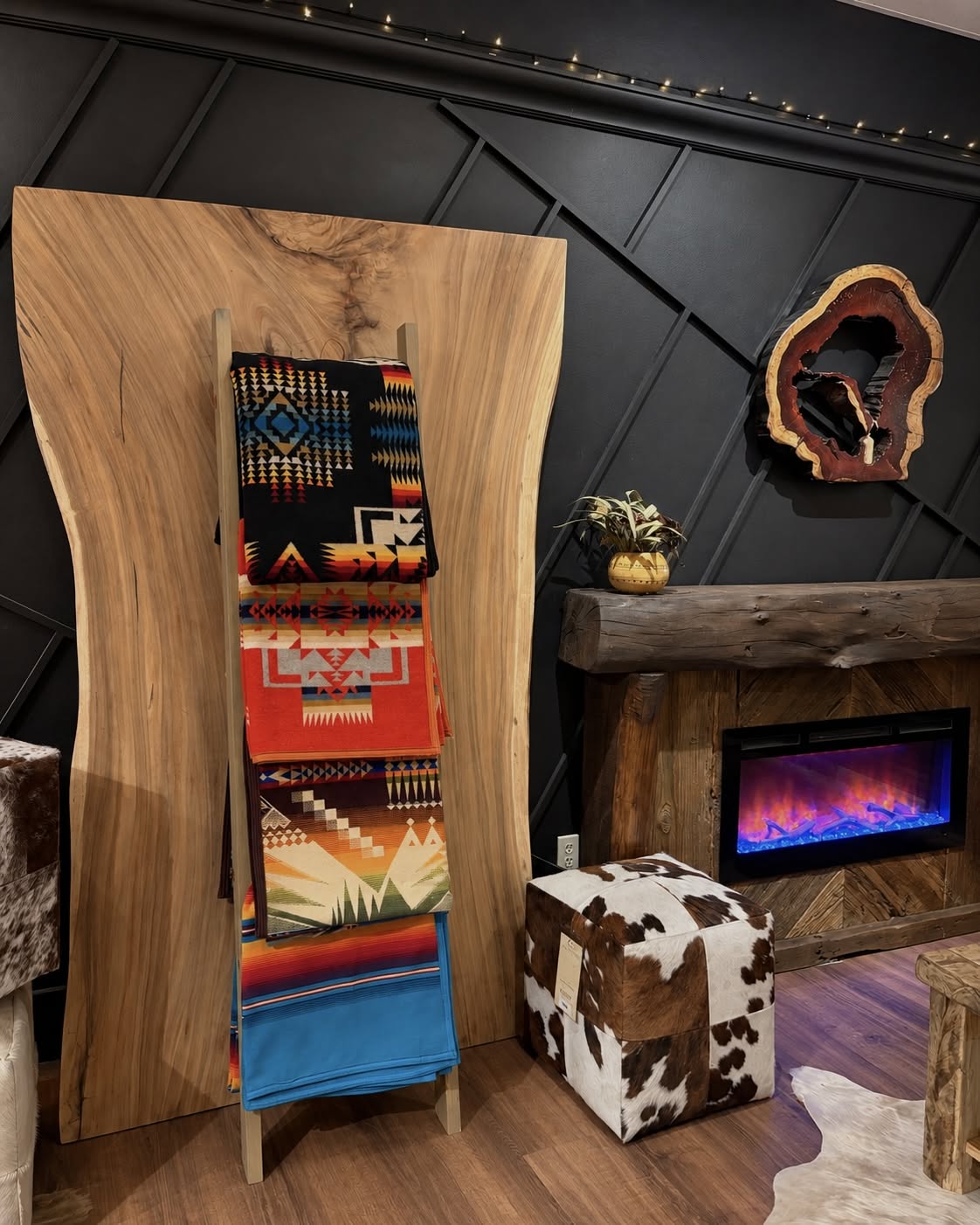 Red-orange Southwestern blanket on the second rung of a wooden display ladder beside a rustic fireplace, with other blankets.