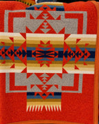 Red-orange Pendleton blanket with blue, navy, gold, cream, and gray Southwestern geometric patterns and orange edging.