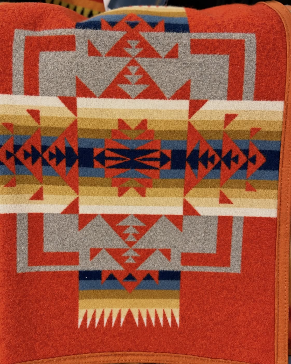 Red-orange Pendleton blanket with blue, navy, gold, cream, and gray Southwestern geometric patterns and orange edging.
