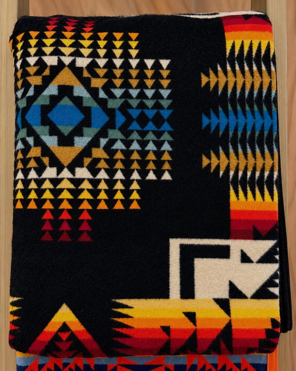 Black Pendleton blanket with turquoise blue, gold, orange, red, and cream geometric patterns.