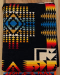 Black Pendleton blanket with turquoise blue, gold, orange, red, and cream geometric patterns.