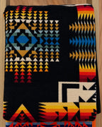 Black Pendleton blanket with turquoise blue, gold, orange, red, and cream geometric patterns.
