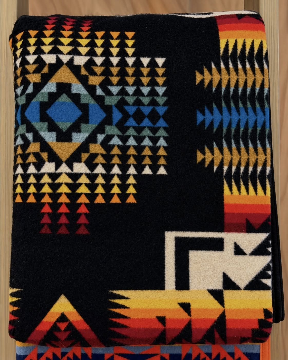 Black Pendleton blanket with turquoise blue, gold, orange, red, and cream geometric patterns.