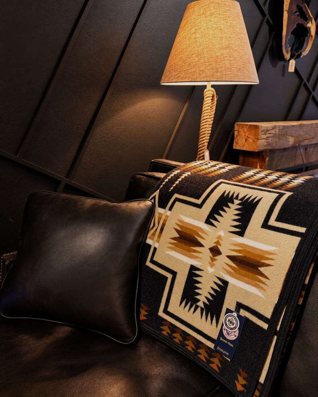 Pendleton Beaver State blanket with black, cream, tan, and brown Southwestern geometric pattern draped over a dark leather sofa.