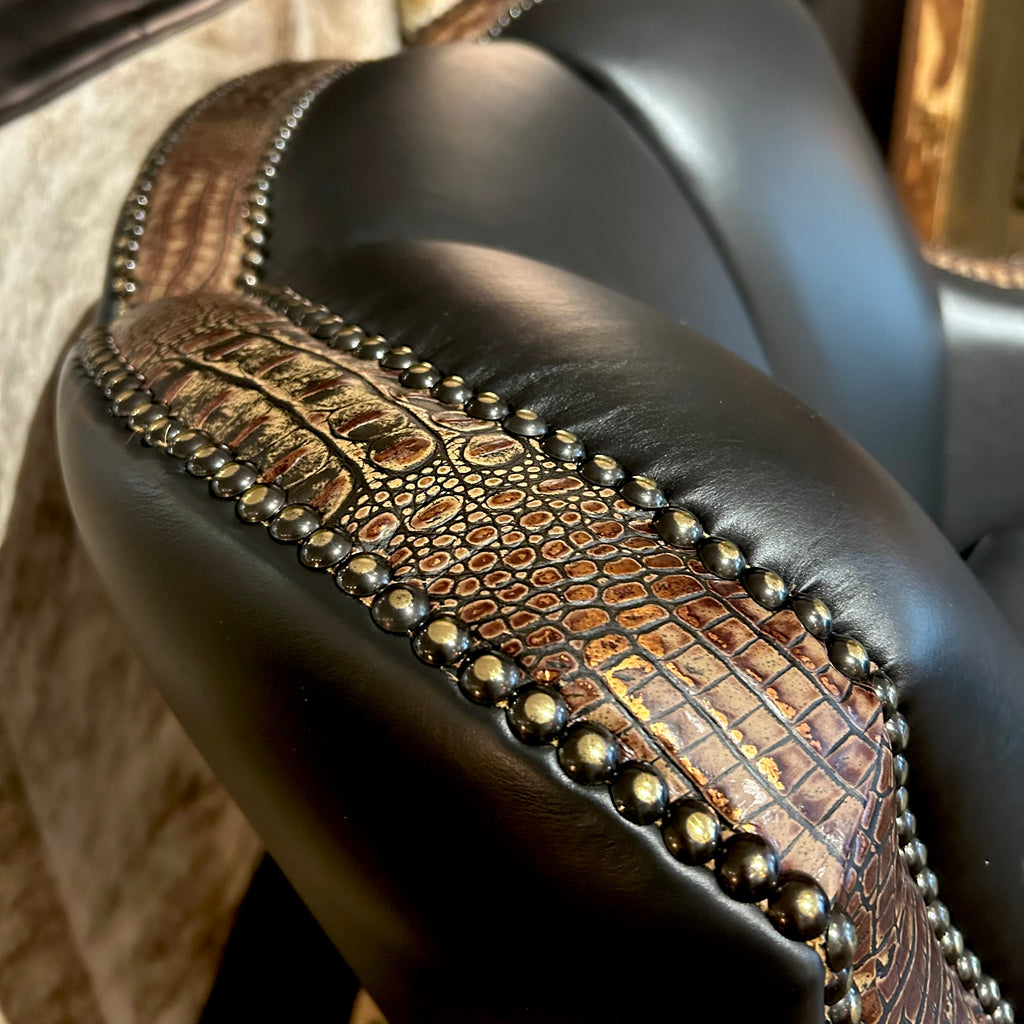 Close-up of a leather swivel glider with decorative nail heads and embossed croc accents.