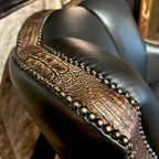 Close-up of a leather swivel glider with decorative nail heads and embossed croc accents.