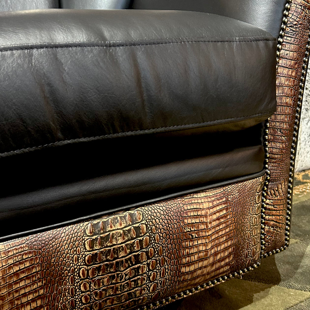 Close-up of a black leather armchair with brown crocodile embossed leather accents.