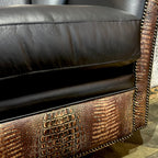 Close-up of a black leather armchair with brown crocodile embossed leather accents.