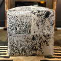 Cube-shaped ottoman with black and white cow print pattern on a patterned rug.