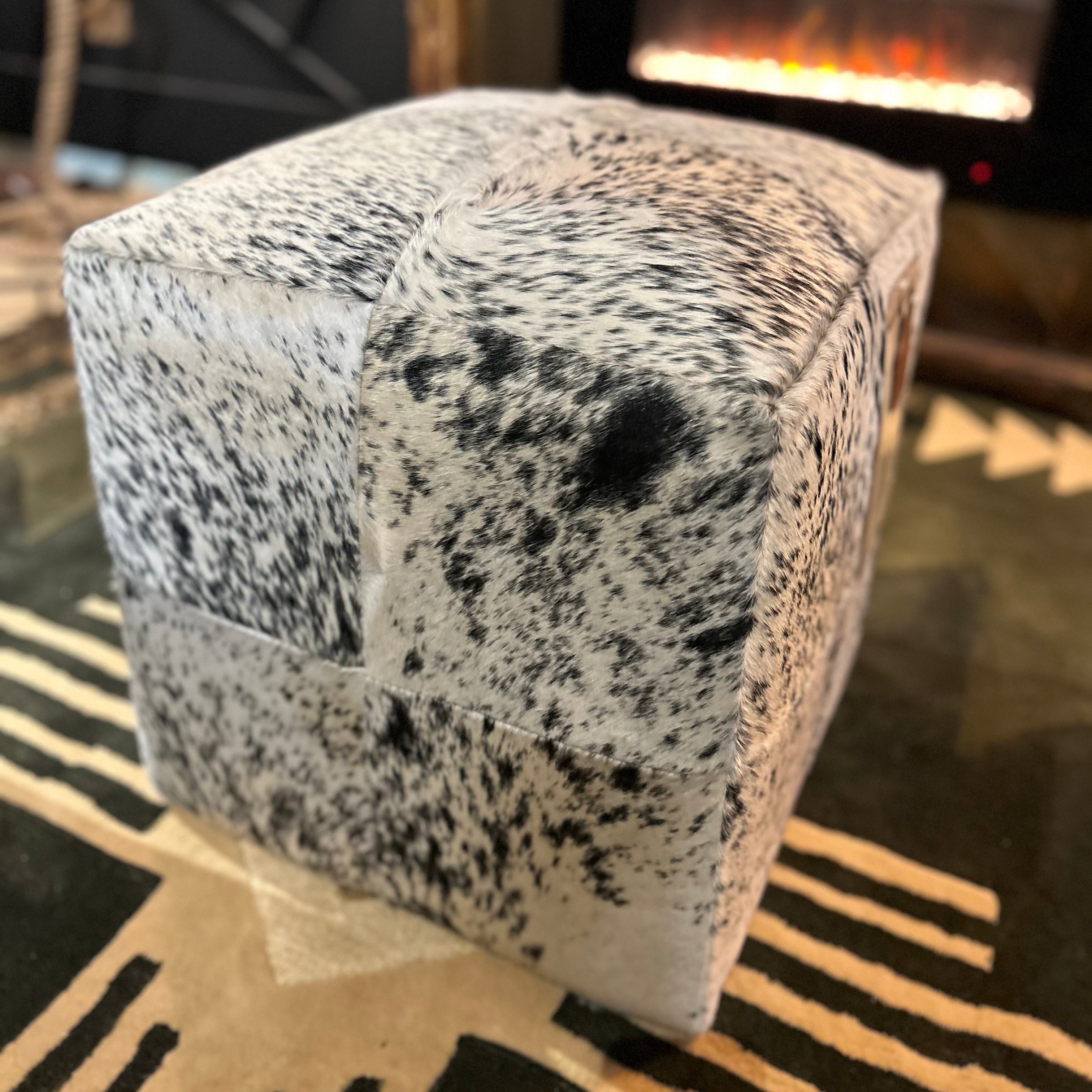 Speckled gray and black ottoman on a patterned rug with a blurred background