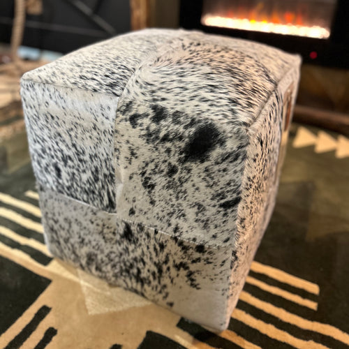 Speckled gray and black ottoman on a patterned rug with a blurred background