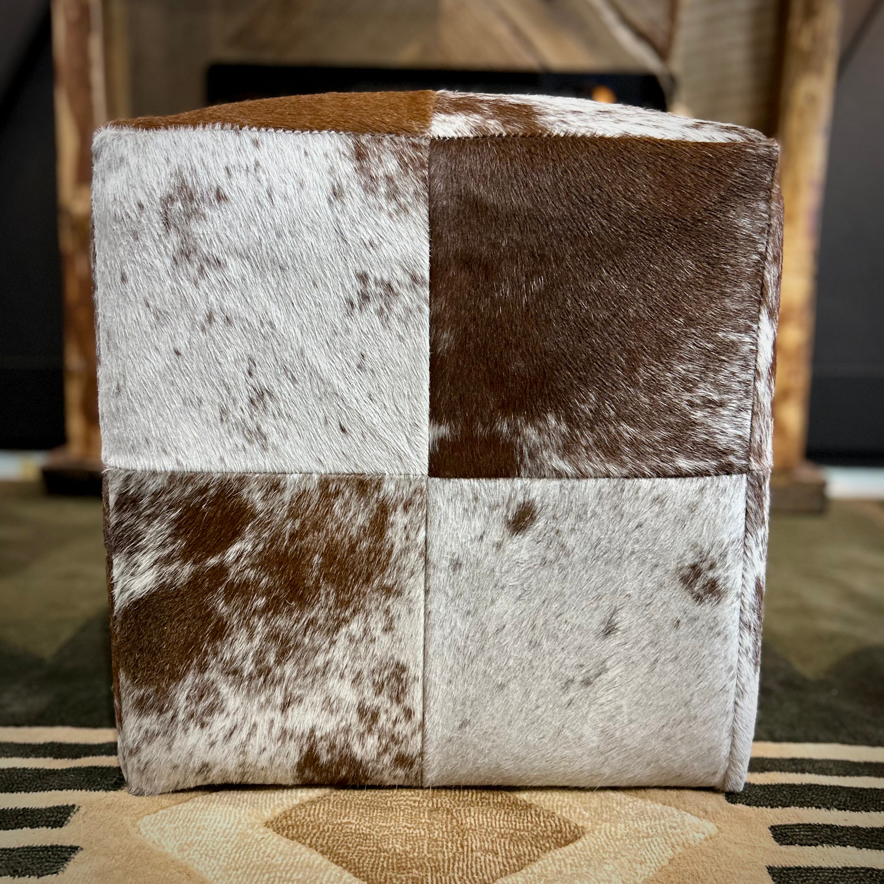Cube-shaped ottoman with checkered cowhide pattern on a rug
