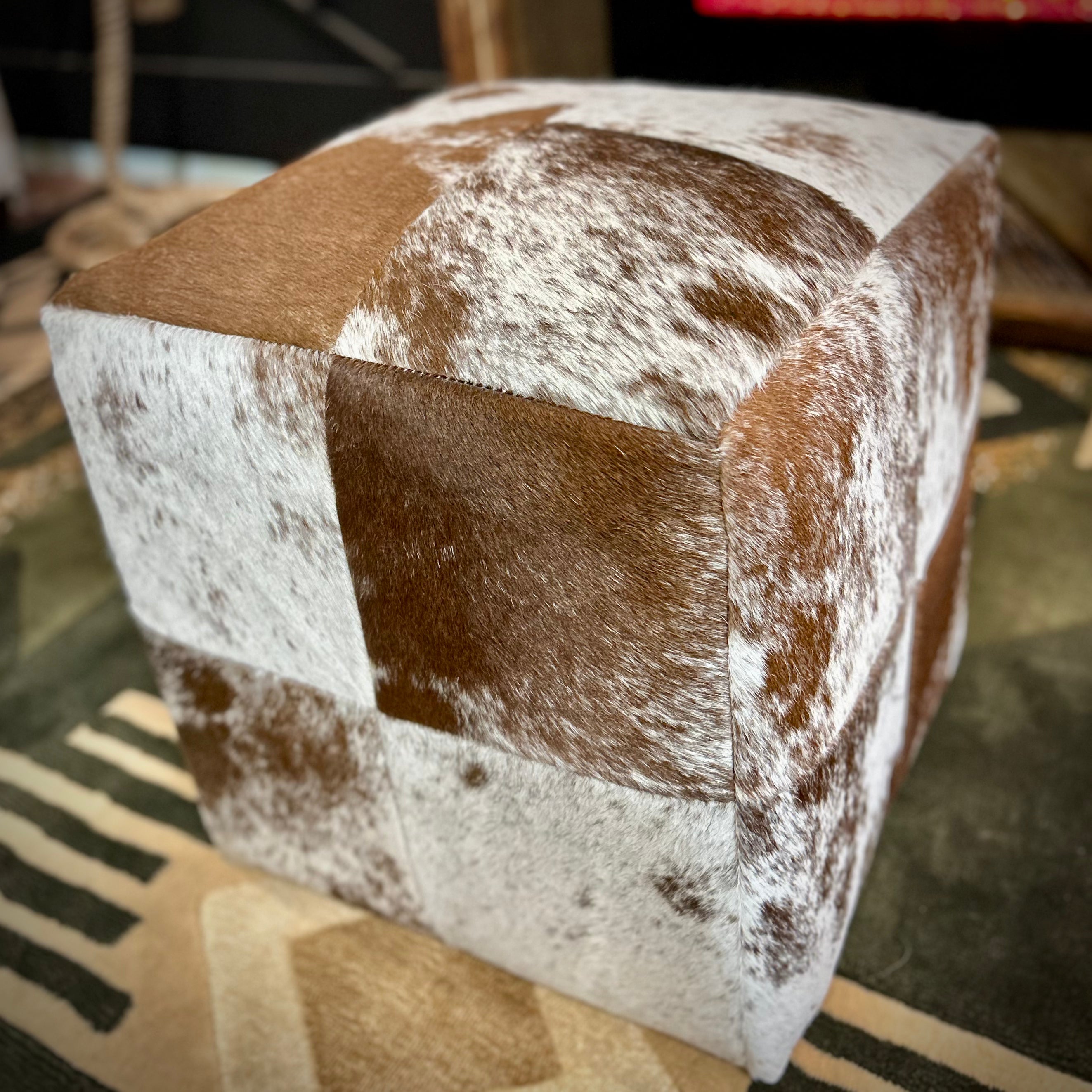 Cube-shaped ottoman with brown and white cowhide pattern on a rug