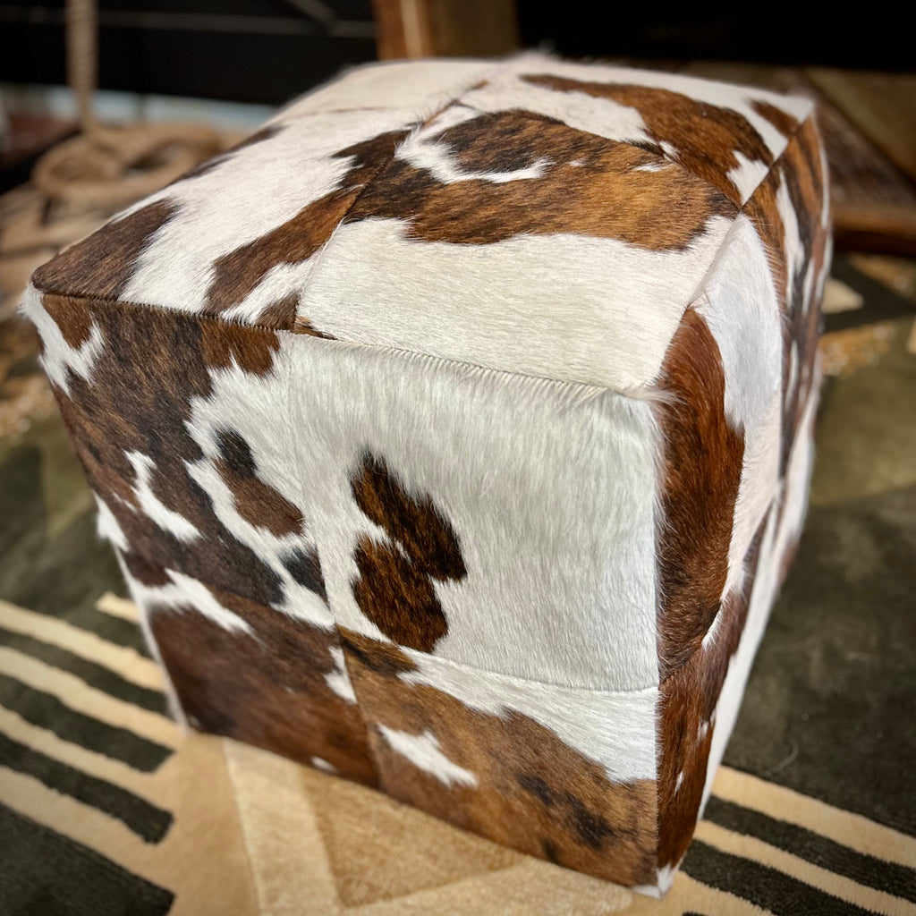 Cube-shaped ottoman with cowhide pattern on a patterned rug