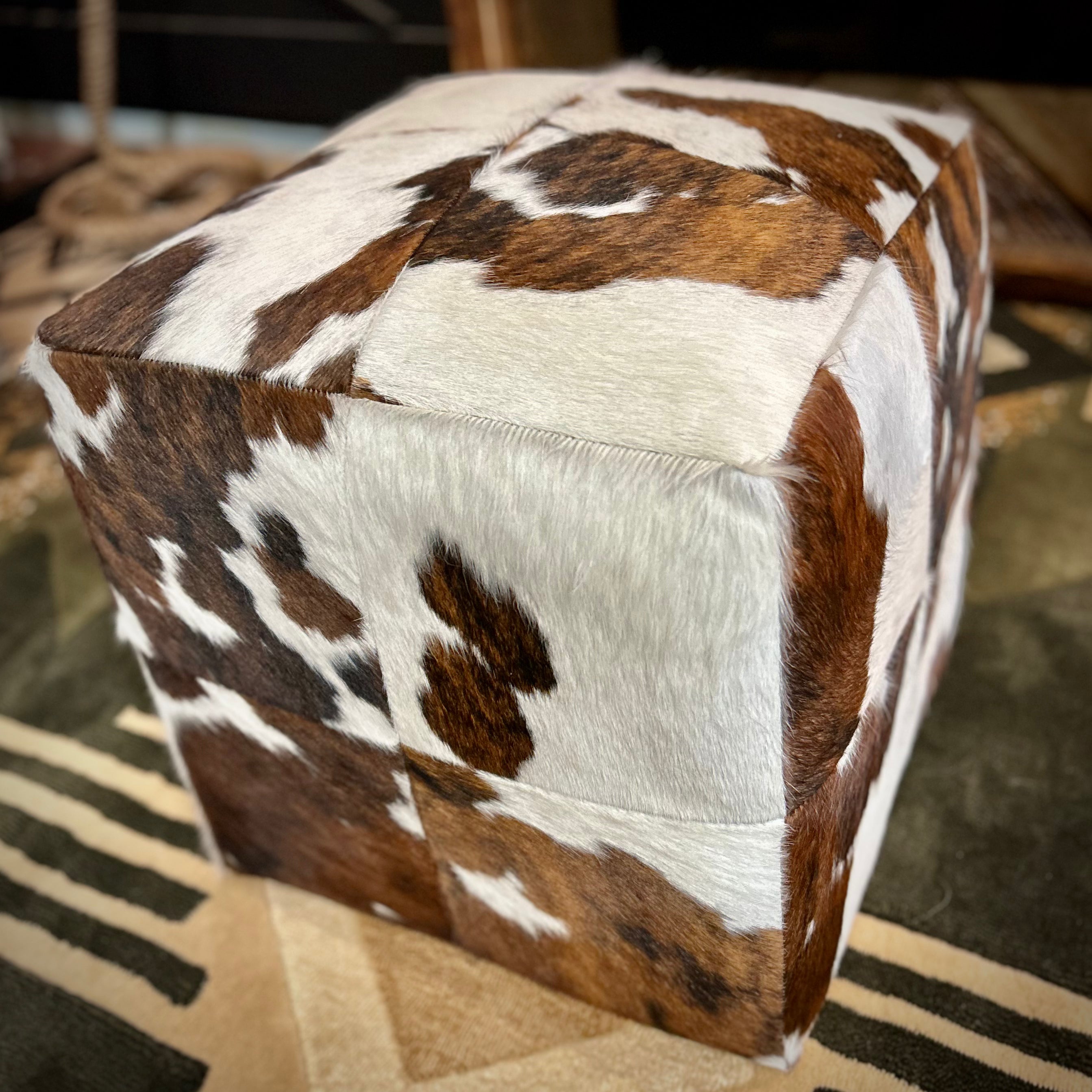 Cube-shaped ottoman with cowhide pattern on a patterned rug