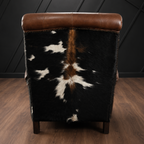 Recliner with cowhide and brown leather backrest against a dark wall.