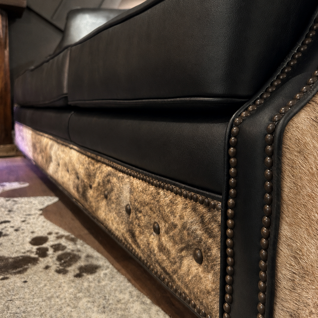 Close-up of a black leather sofa with brindle cowhide pattern and nailhead trim.