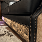 Close-up of a black leather sofa with brindle cowhide pattern and nailhead trim.