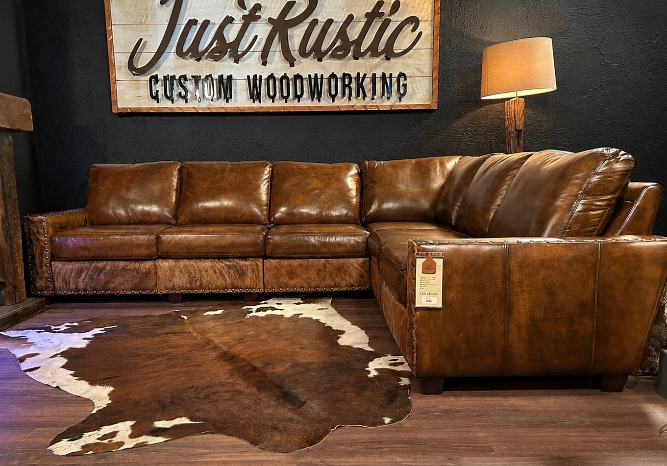 Brown leather sectional sofa in a room with a cowhide rug and 'Just Rustic Custom Woodworking' sign.