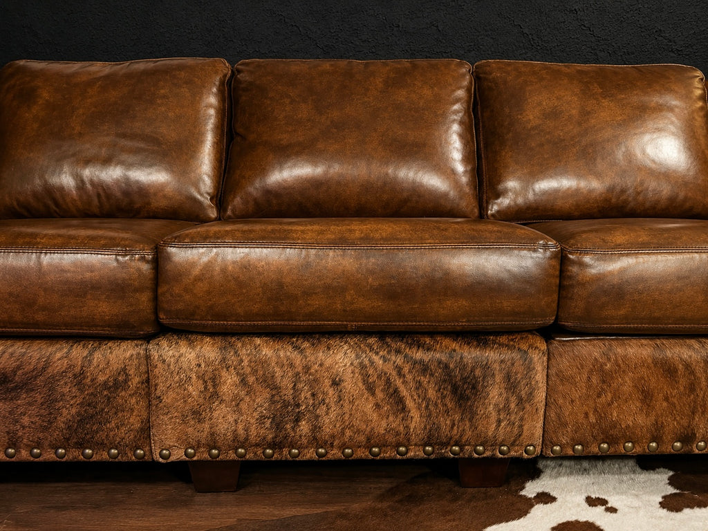 Brown leather sofa with nailhead trim against a dark wall.
