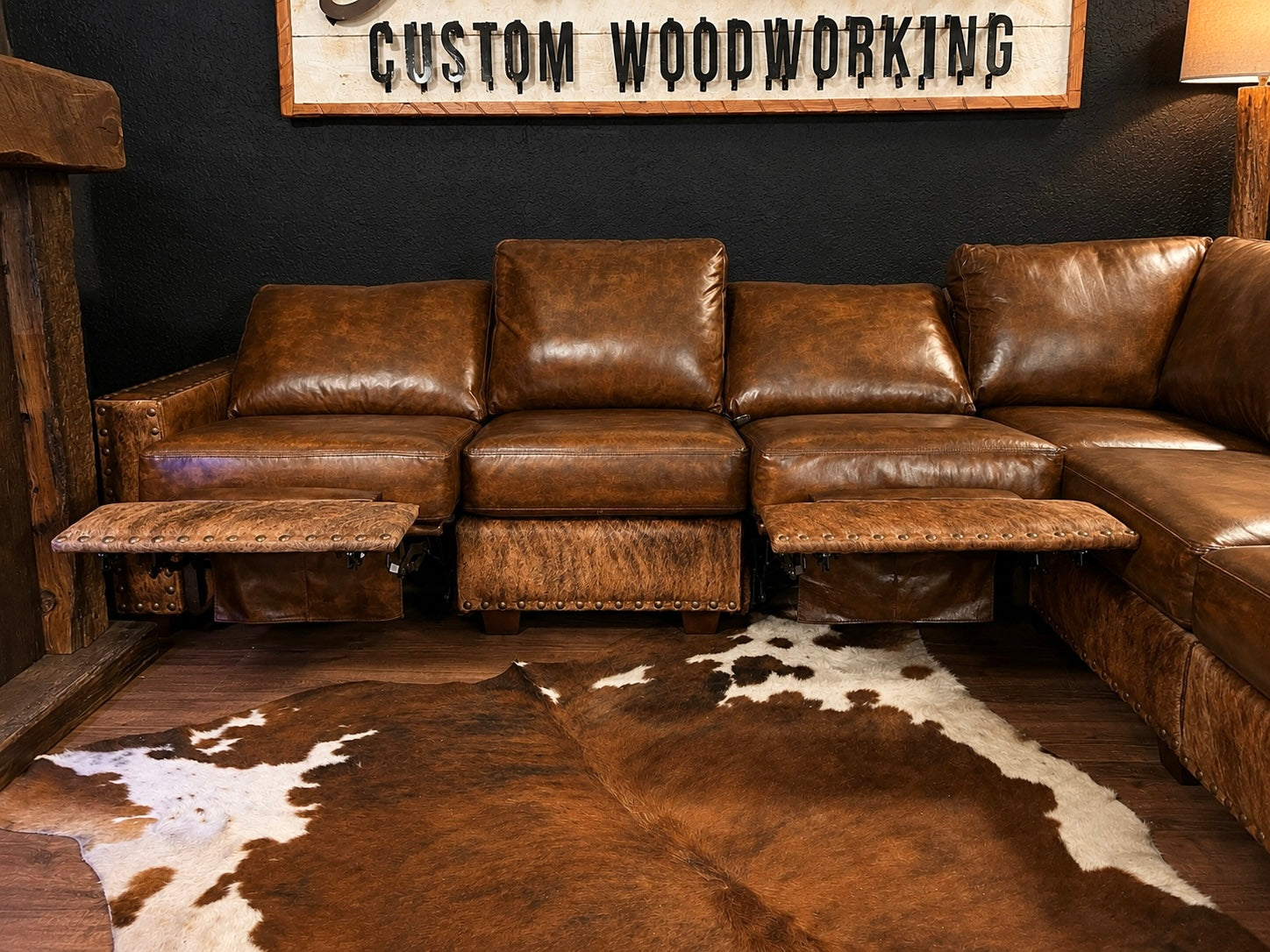 Brown leather sectional sofa in a room with a cowhide rug and 'Custom Woodworking' sign.