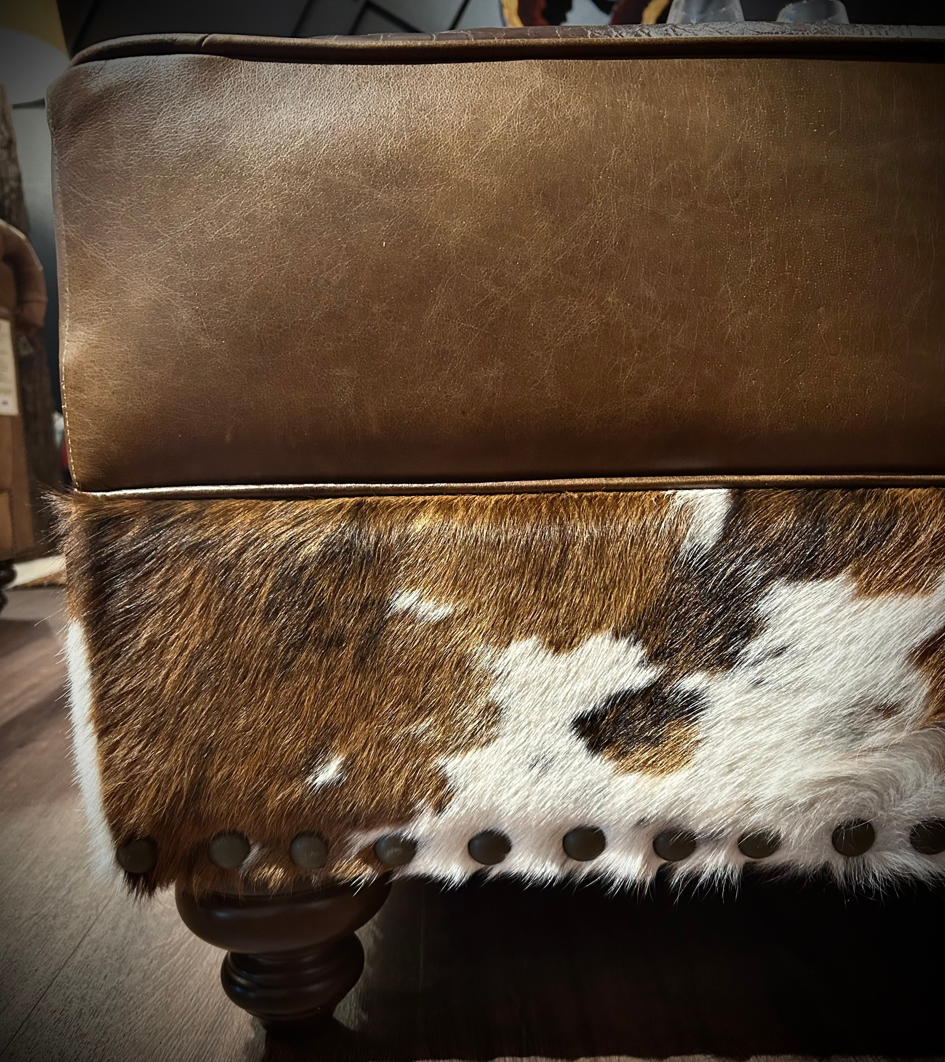 Brown leather ottoman with cowhide pattern on a wooden floor.