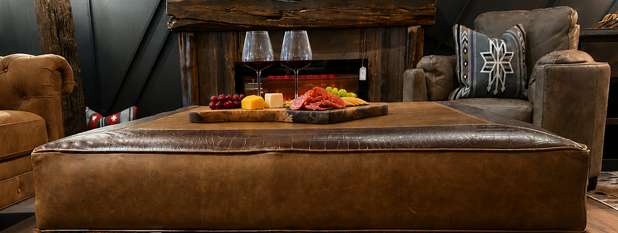 Oversized leather and cowhide ottoman with a charcuterie board and wine glasses on top.