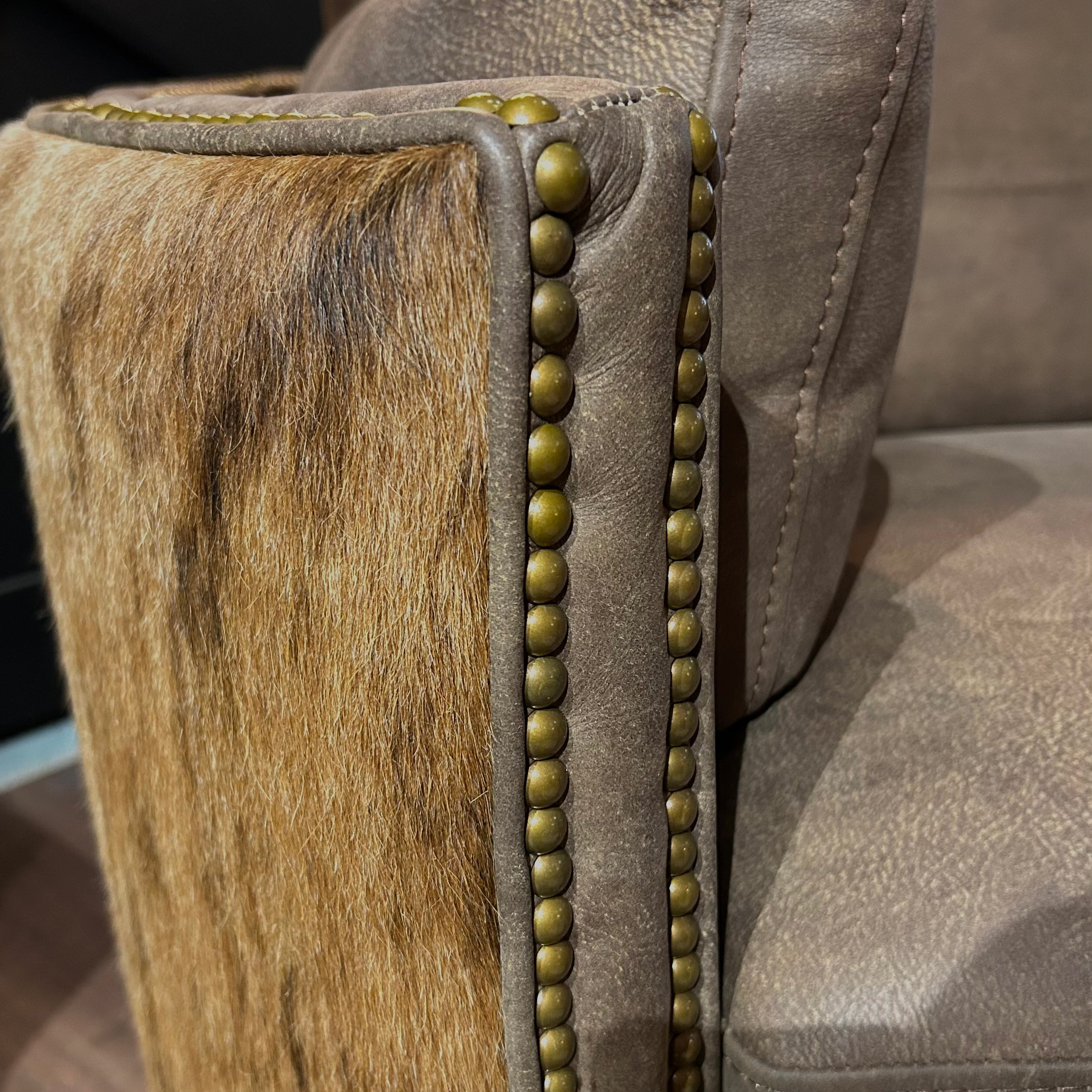 Close-up of a brown leather armchair with brass nailhead accents and cowhide arms.