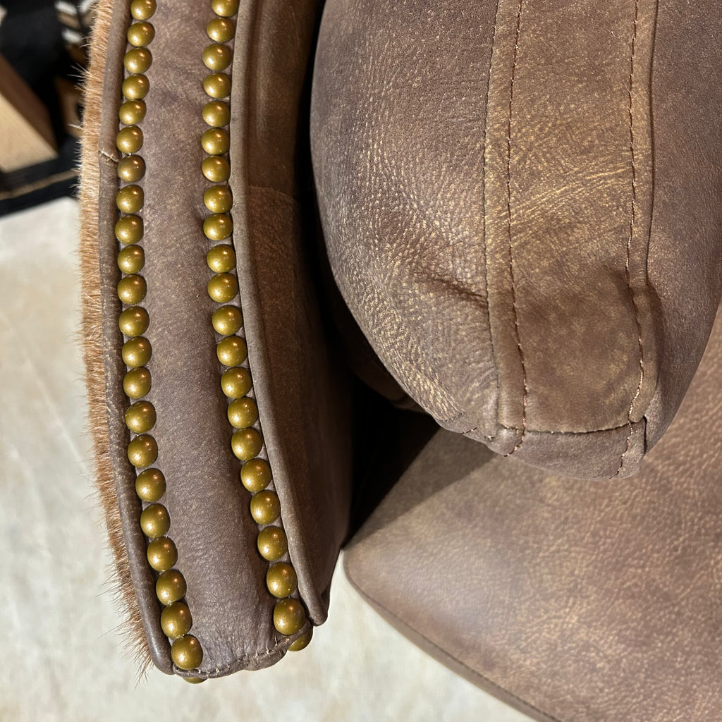 Close-up of brown leather chair with brass nailhead accents.