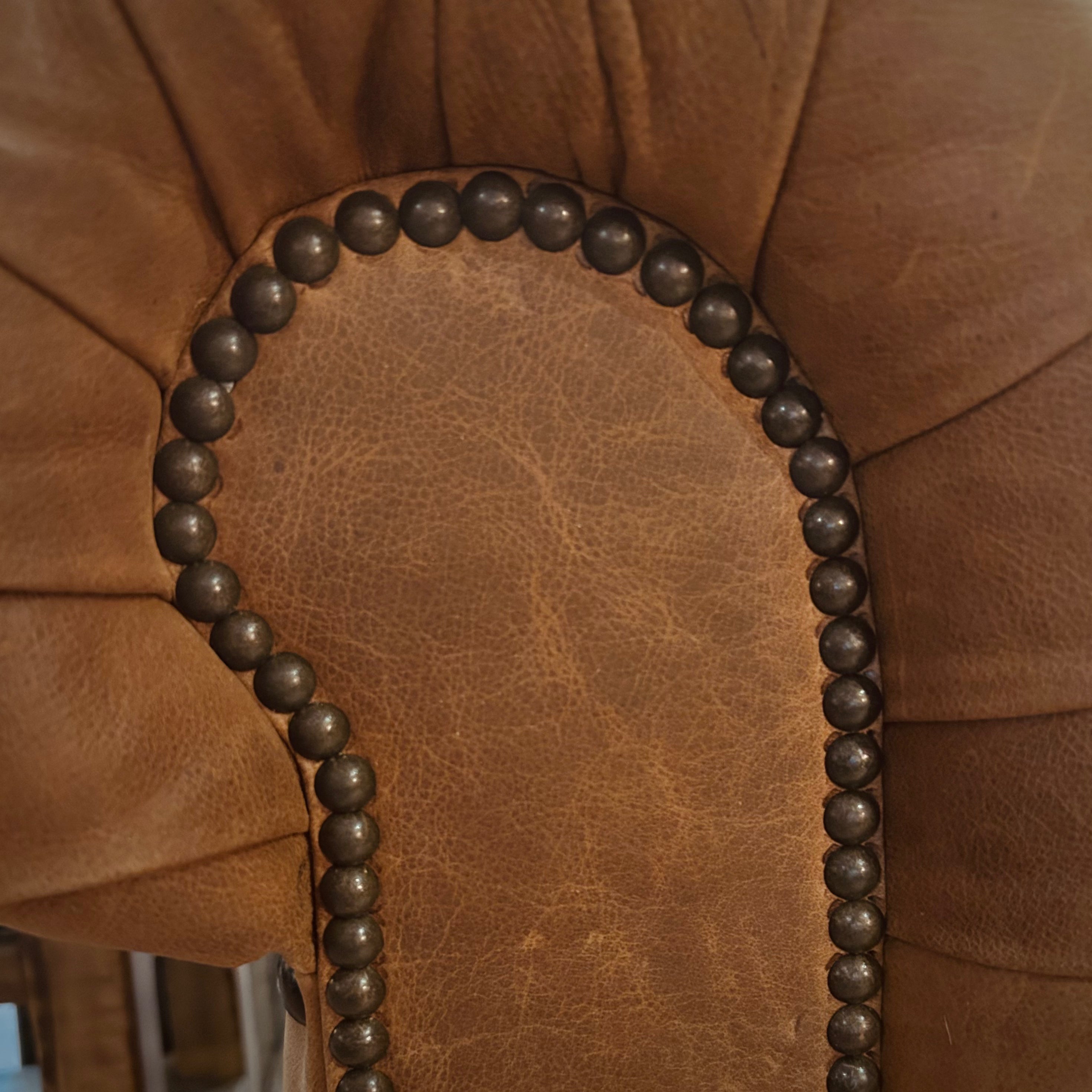 Close-up of a brown leather sofa with a nailhead accent on the arm.