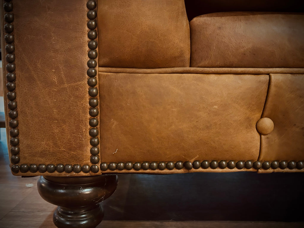 Close-up of a brown leather sofa with nailhead trim