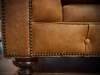 Close-up of a brown leather sofa with nailhead trim