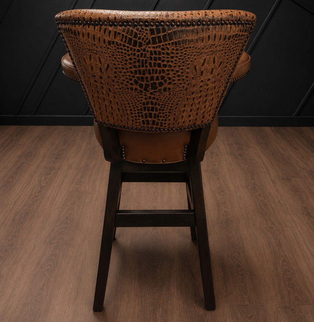 Brown leather barstool with embossed crocodile accents against a black paneled wall.