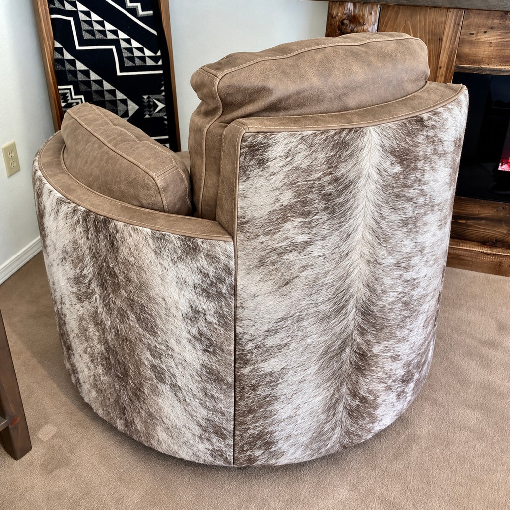 A round swivel recliner with a brindle cowhide-patterned seat and back, and gray leather armrests and back cushions, shown in a home interior setting.