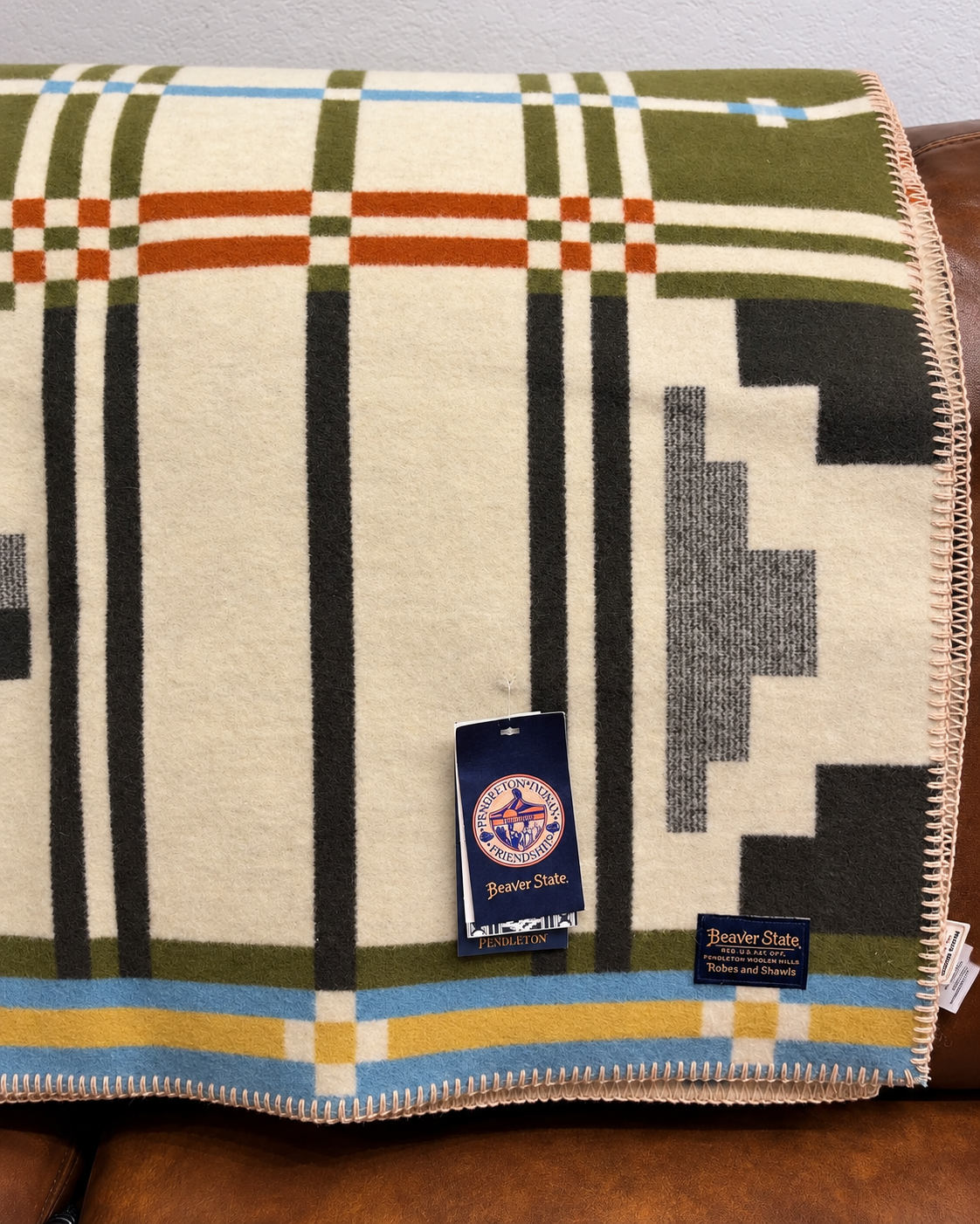 Pendleton Beaver State olive and cream plaid blanket with charcoal geometric accents, rust stripes, blue and gold bands, and stitched edges