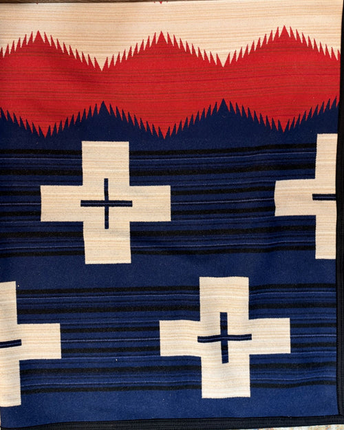 Western blanket showing cream cross motifs on navy with a red sawtooth band and black binding