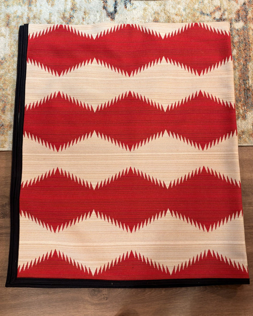 Western geometric blanket showing red sawtooth bands across cream with black binding