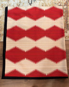 Western geometric blanket showing red sawtooth bands across cream with black binding